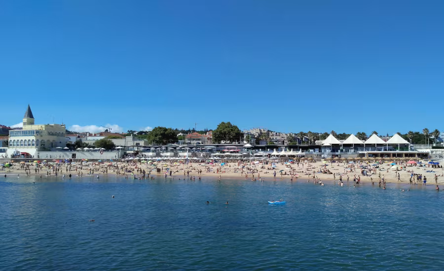 Crowded Estoril beach with swimmers, umbrellas and seaside buildings
