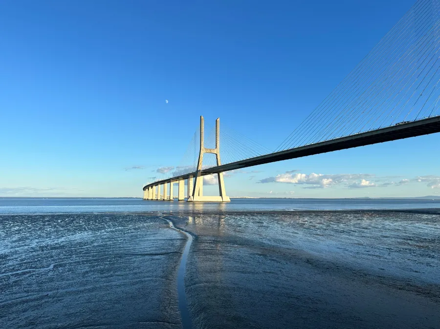 Vasco da Gama bridge: Large cable‑stayed bridge over shallow water under a blue sky with the moon