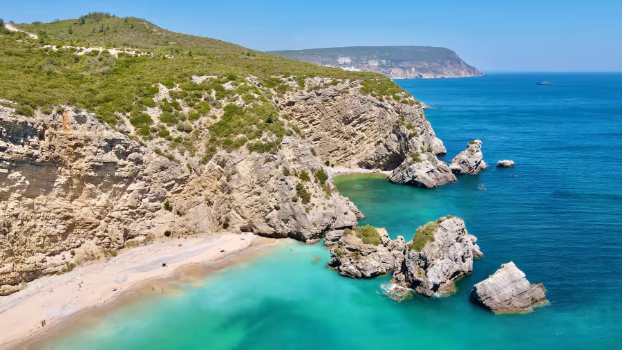 Sesimbra beach with steep cliffs, turquoise water and a small sandy cove