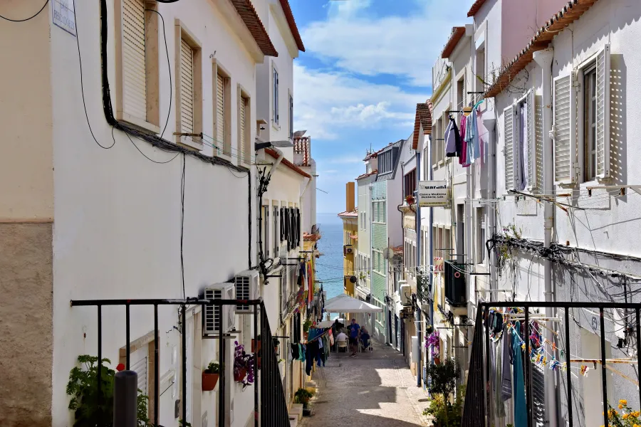 Sesimbra narrow sloping street with pastel houses, hanging laundry and a sea view at the end