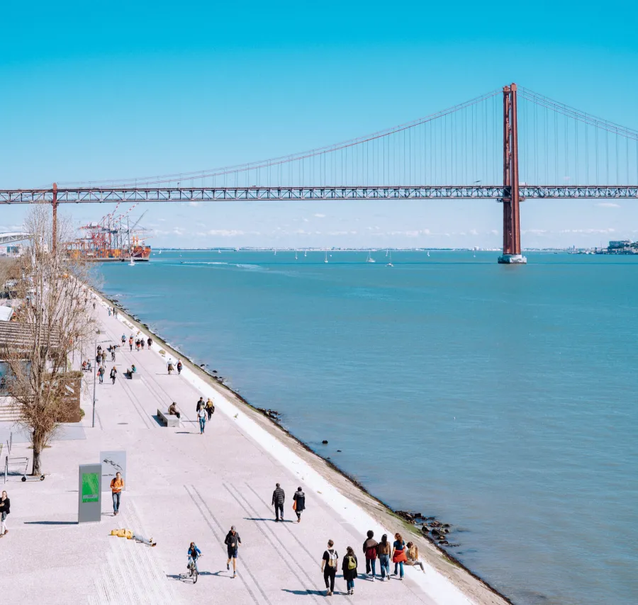 Waterfront promenade with people and the red suspension bridge