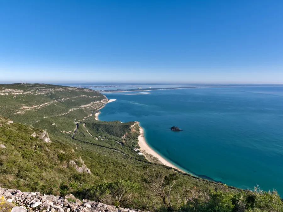 Wide Arrábida bay with steep green hills, clear blue water and a small rocky island