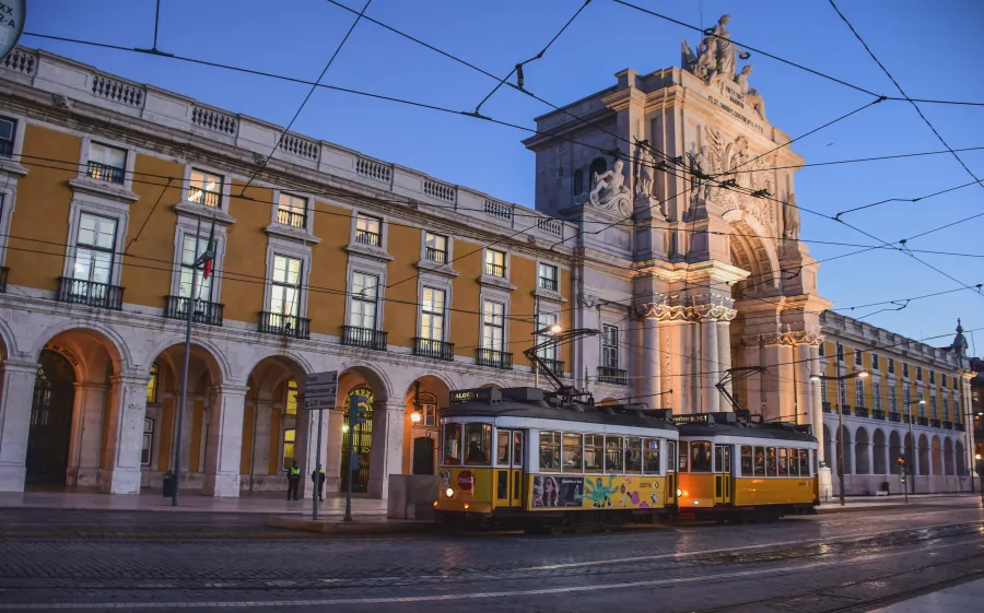Yellow tram passing under Lisbon’s illuminated triumphal arch at dusk